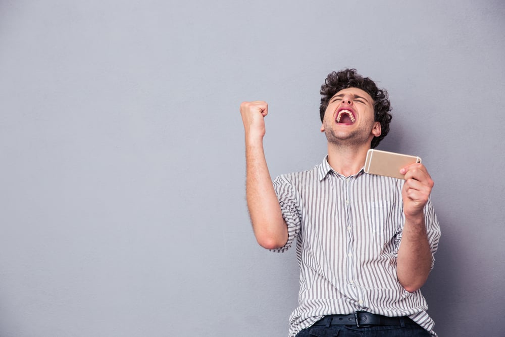 Happy man holding smartphone and celebrating his success over gray background-1